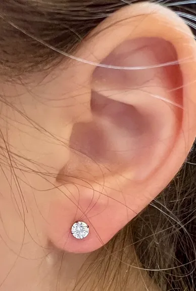 A close-up image showing an ear with a newly pierced earlobe and a sparkling stud earring